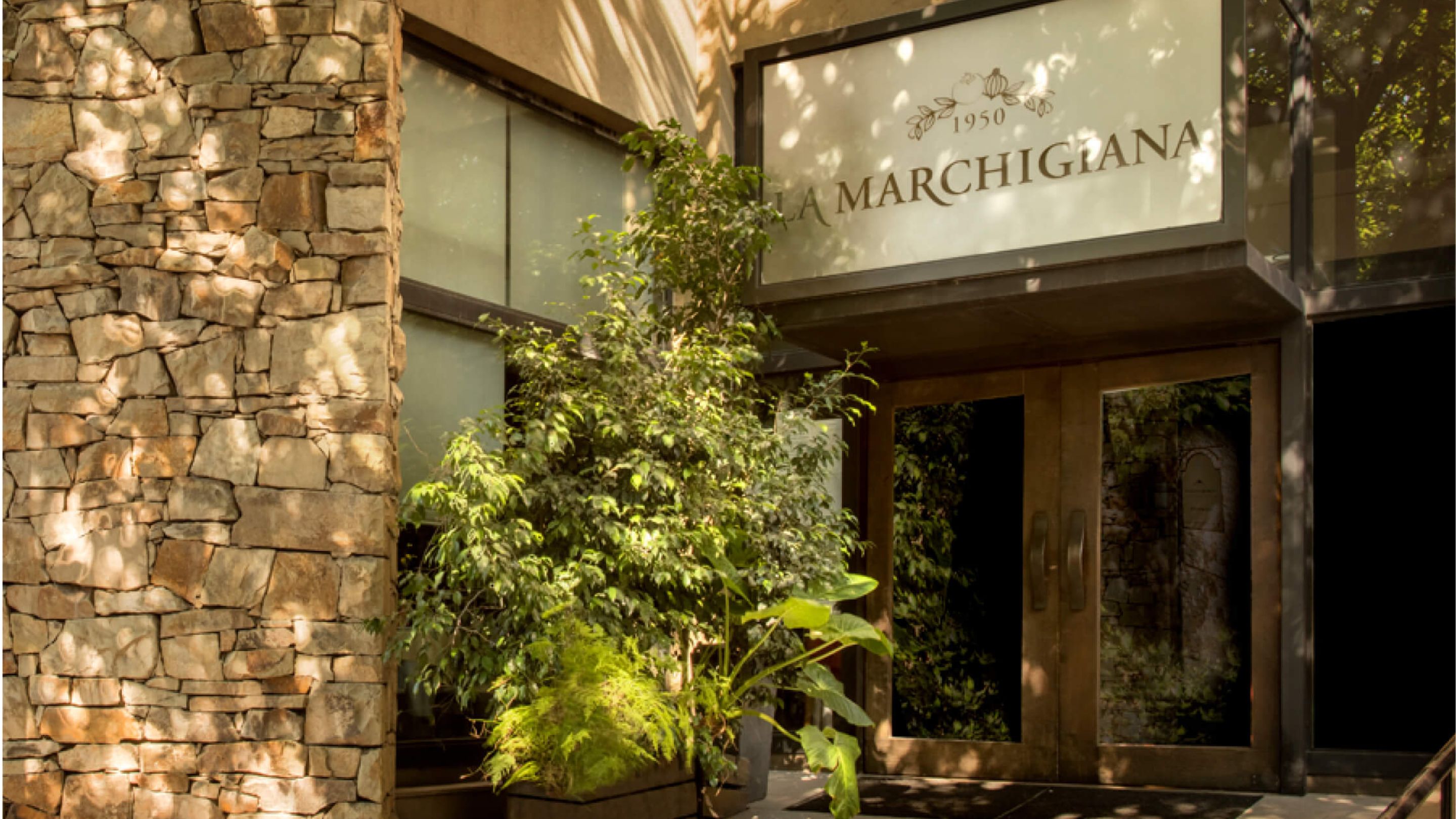 Entrada de La Marchigiana Centro, con pared de piedra y vegetación